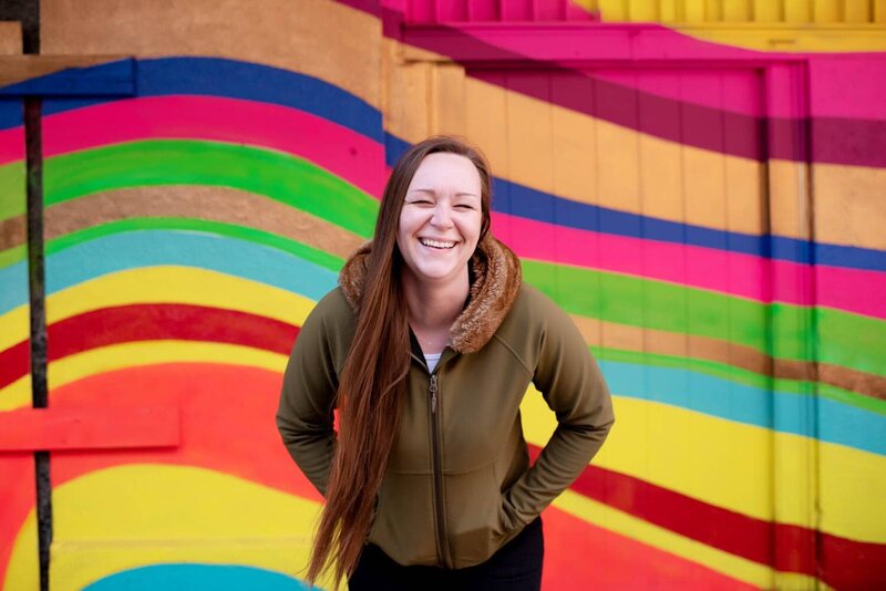 a woman laughs in front of a brightly colored wall with neon waves