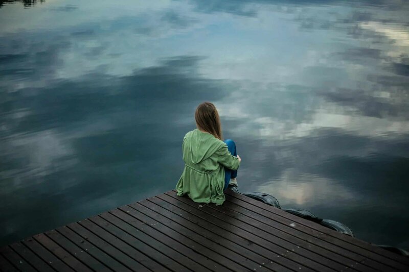 Picture of a woman sitting at the edge of a deck and looking out at te river