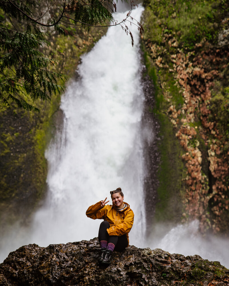 Mattie Nelson- Elopement Photographer sitting in front of Wahclella Falls in Oregon.