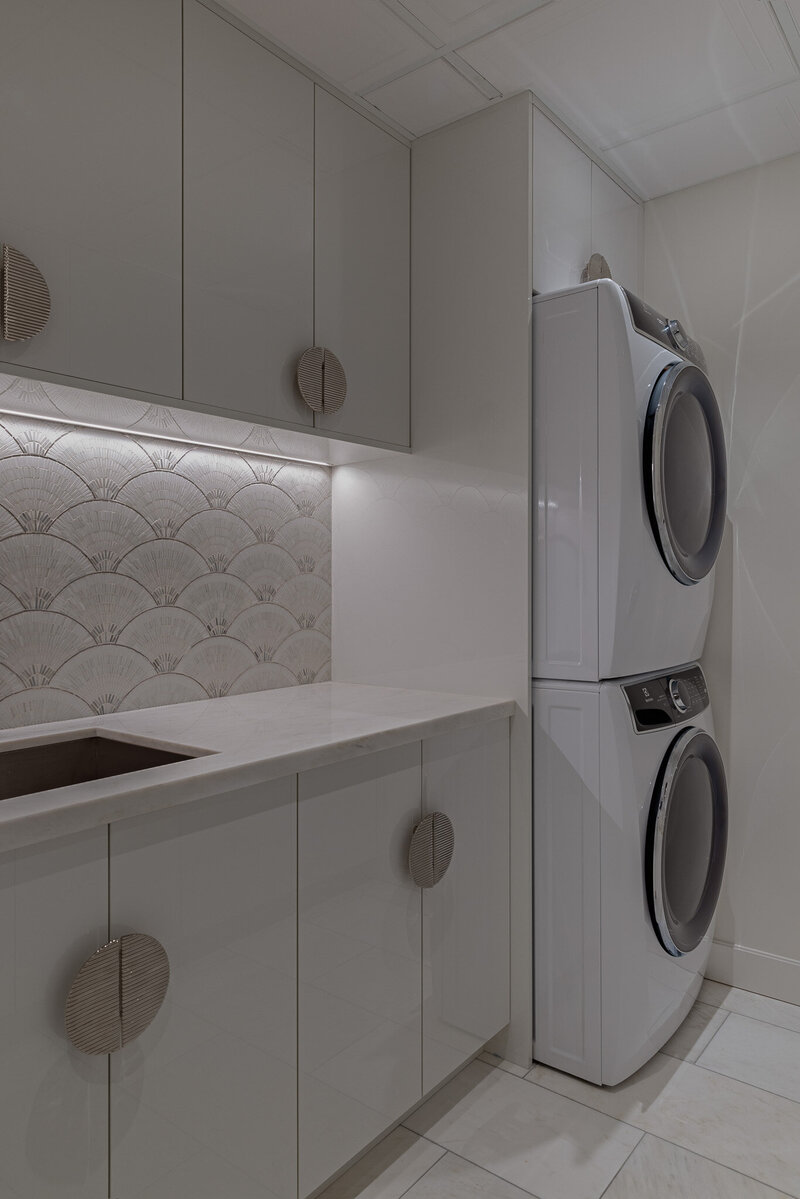 Sleek modern laundry room with mosaic backsplash, textured handles and white cabinetry by Sister Studio.