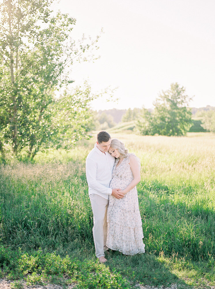 Mother and father look down at bump on beautiful spring day, photographed by Edmonton maternity photographer, Kahla Kristen