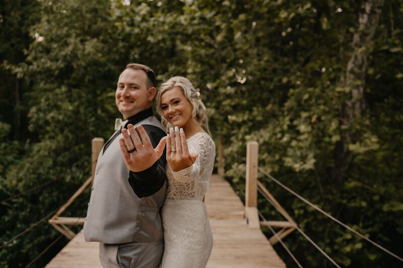 Newlyweds showing off their wedding rings on a wooden bridge