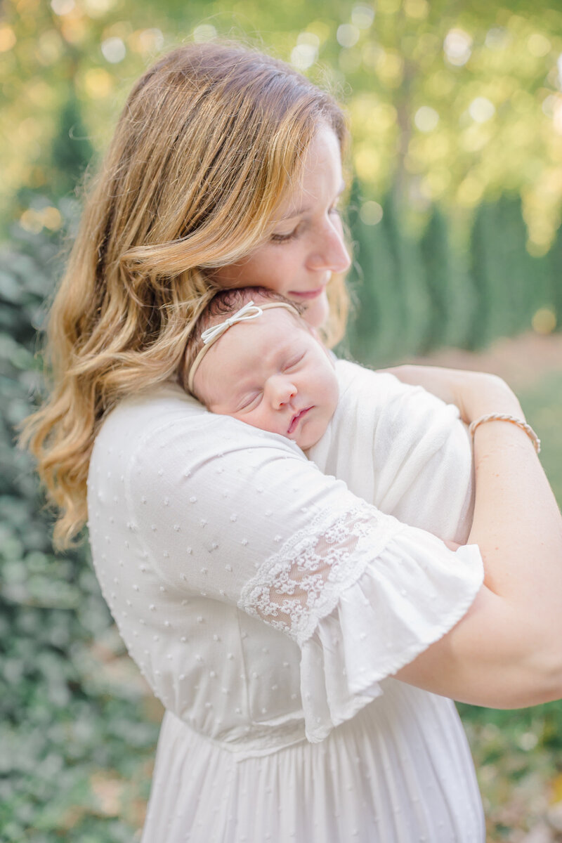 A mother gently holds her newborn on her shoulder, embracing her baby with love while her eyes are closed. The soft, natural light highlights the warmth and intimacy of the moment. Captured by Connecticut newborn photographer, this image reflects the deep bond between mother and child.
