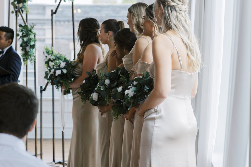 Ceremony photos of bridesmaids in beige satin dresses taken by Allexx B Photography at Upper East in Kenosha, WI