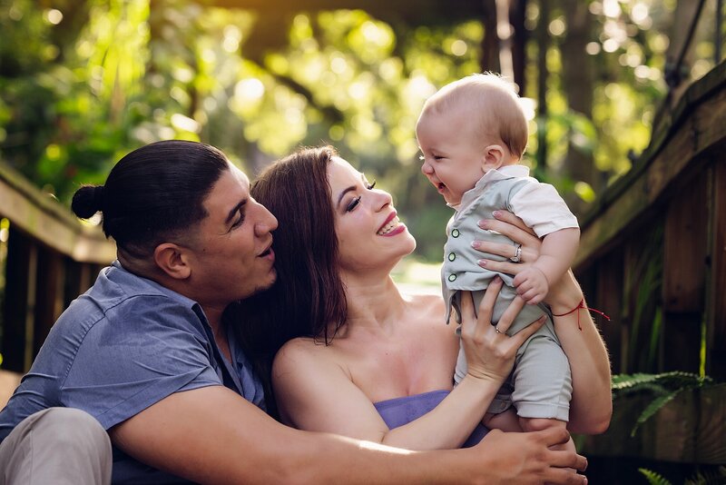 A smiling couple holds their baby, radiating joy and love in a warm family moment.