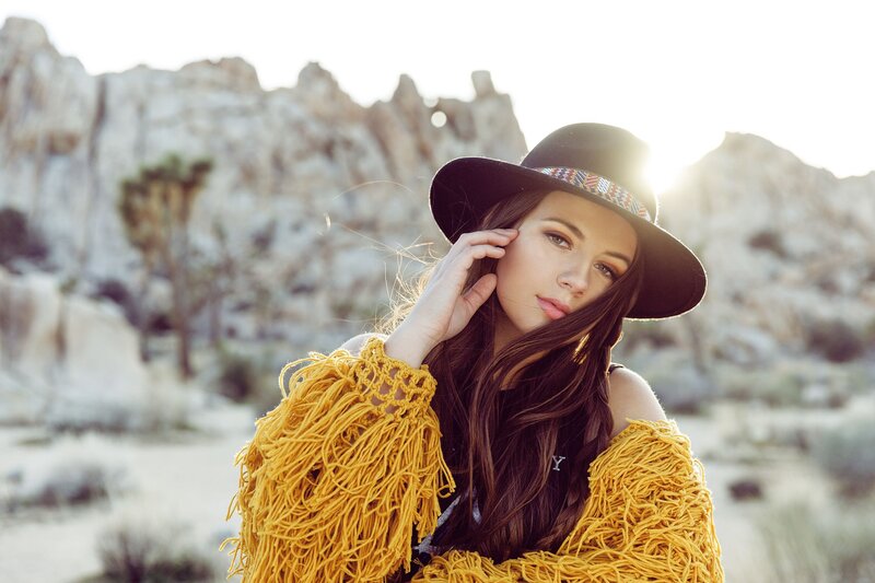 Boho teen model in a mustard fringe jacket and wide-brim hat posing at golden hour in Joshua Tree – photographed during a creative photography workshop.