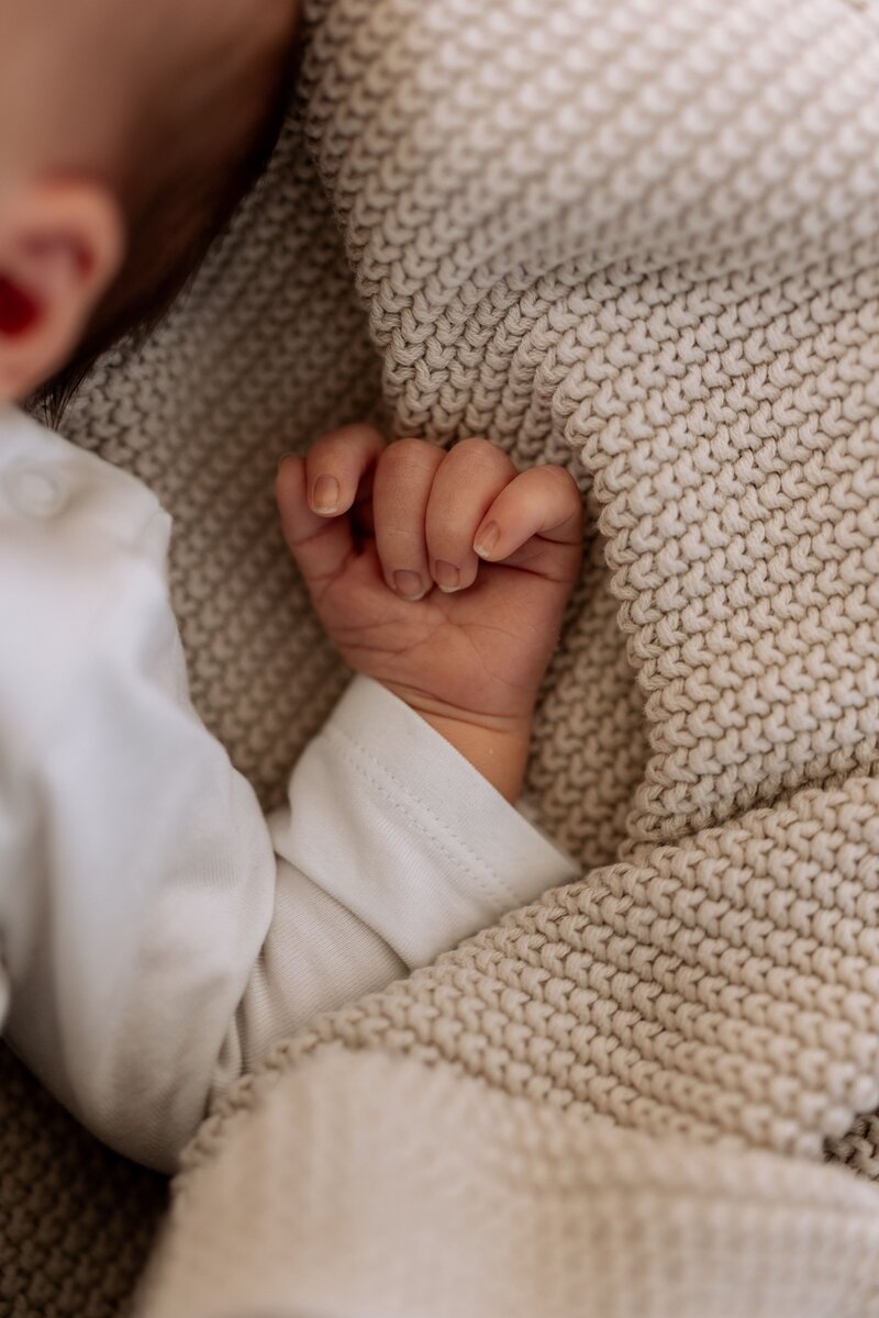 Detailfoto von einer kleinen Babyhand auf beigen Strickuntergrund