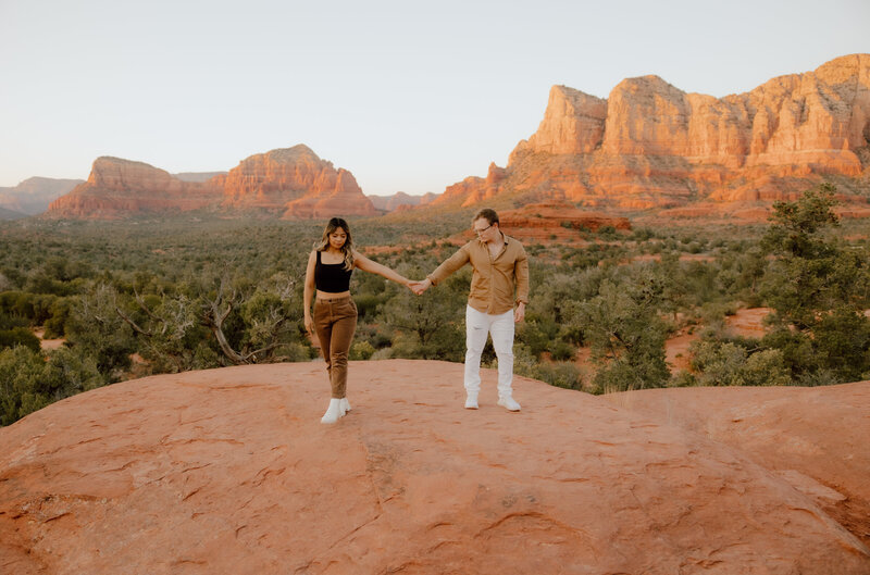 couple holding hands on top of mountainside in the desert