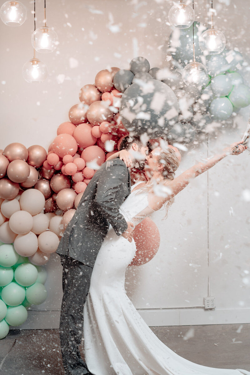 Bride and groom celebrating under a ballon arch  with first kiss
