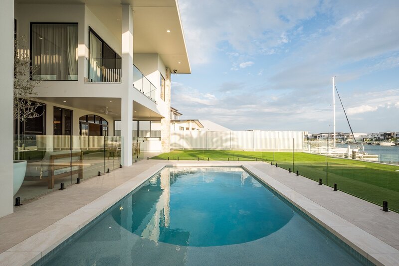 A modern luxury home by NXTgen Construction featuring a sleek, glass-enclosed pool with a distinctive curved entry step and waterfront views.