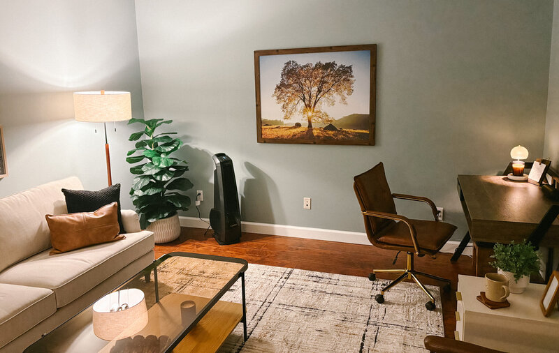Counseling office with sofa, desk, and framed tree artwork, designed as a welcoming therapy space.
