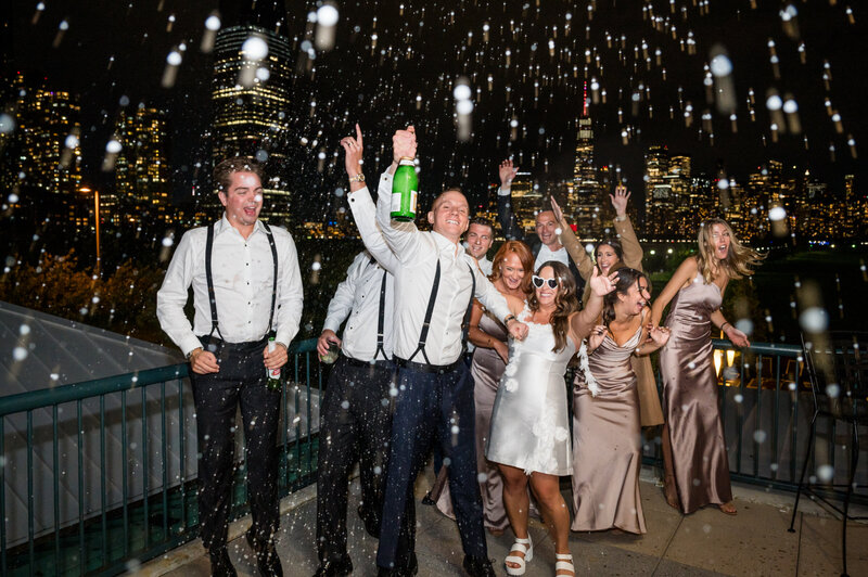 groom spraying champagne on the porch outside of liberty house with the bride and bridal party cheering behind