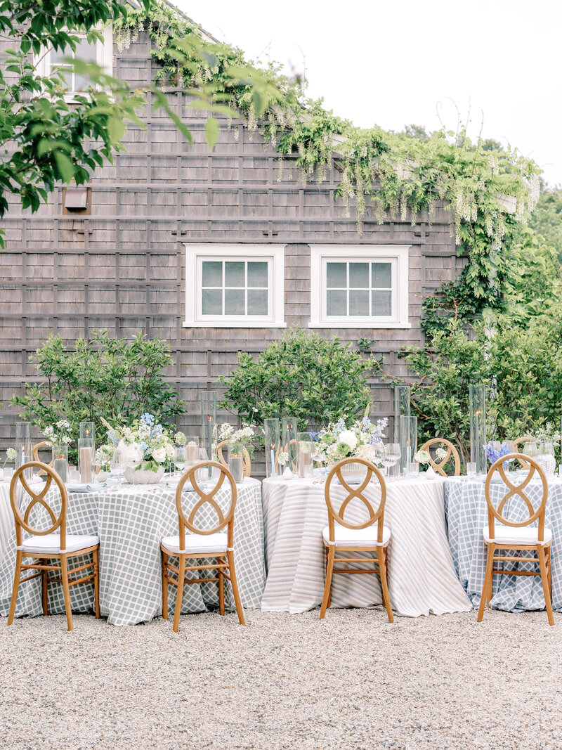 Outdoor reception tables with wood chairs, patterned tablecloths, and floral centerpieces