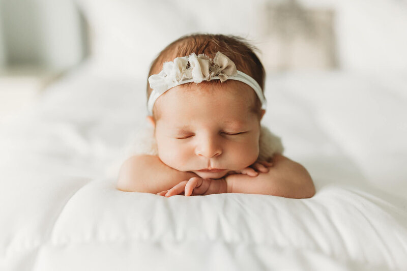 baby boy sleeping with his hands under his head in a green onesie on a green plant background newborn harrisburg photos