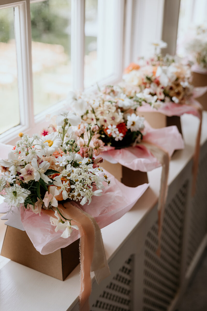 A bride and groom stood on the beach in Cornwall looking at the sea. The bride has flowers in her hair and carrying a large bouquet of peach roses, foliage and succulents