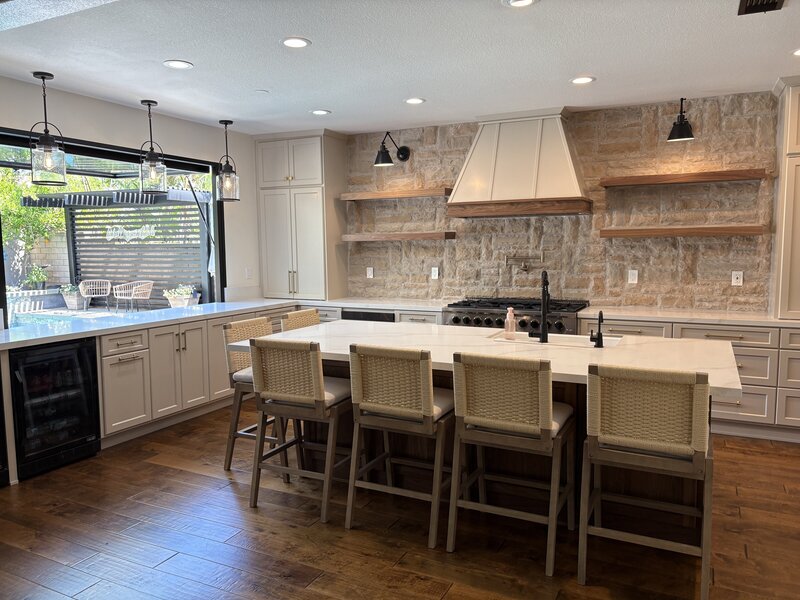 A newly remodeled kitchen white a huge island, a focal wall with stone, and white cabinets.