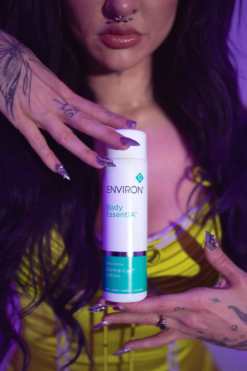 Woman with long nails wearing green dress holds bottle of "Environ"