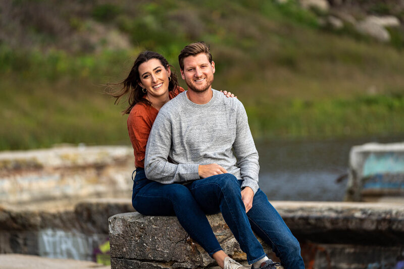 couple smiling and embracing each other on the beach with a large rock in the background