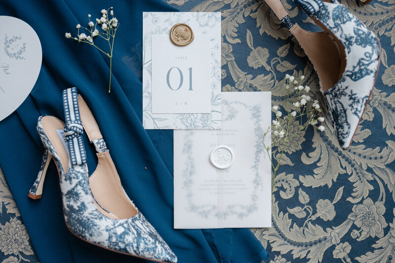Composition lay flat mettant en valeur des souliers de mariée élégants sur un fond marine et or, détail sophistiqué et stylisé d’un mariage chic et moderne