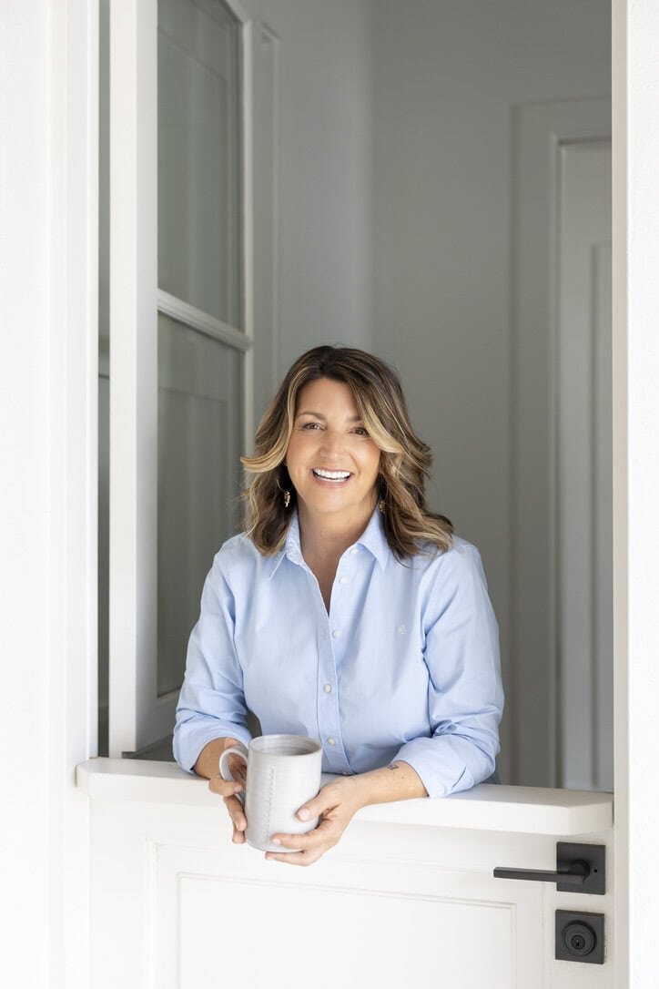 woman in blue leaning on a white dutch door with a mug