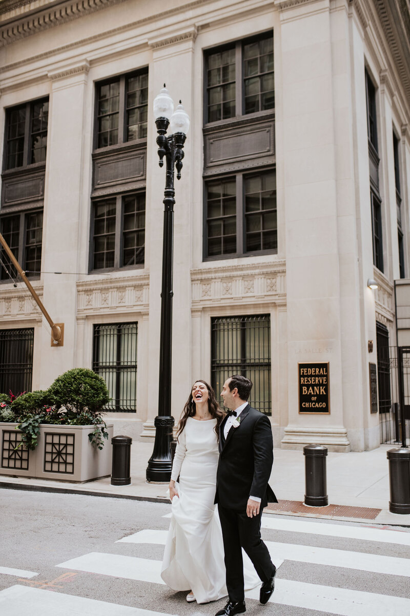 a bride and groom laughing while walking in a downtown area