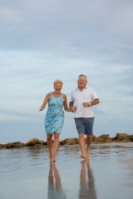 Happy couple running hand-in-hand on St Augustine beach during family photo session, professional family photographer captures joyful moment