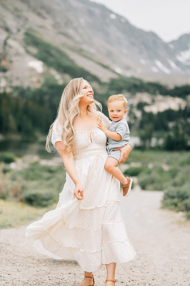 mother holding her son and twirling her dress in front of rocky mountains