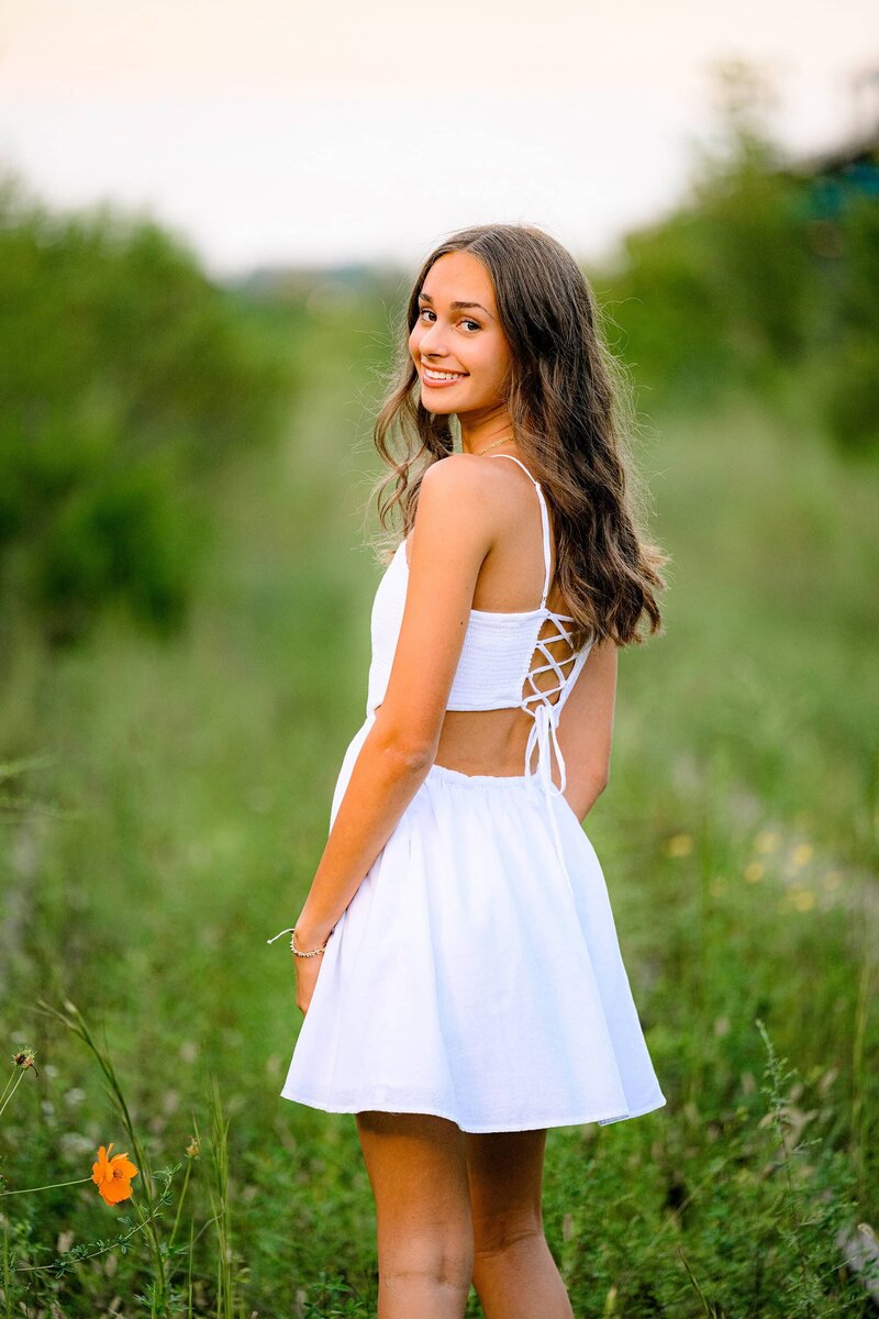 senior wearing white dress looking back over her shoulder 