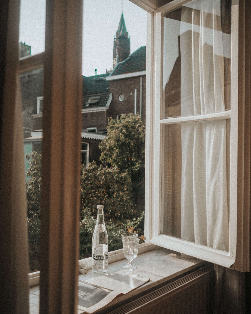 A person holds an empty glass above a manuscript by Phillipa Leseberg on the windowsill, with a bottle of sparkling water nearby.