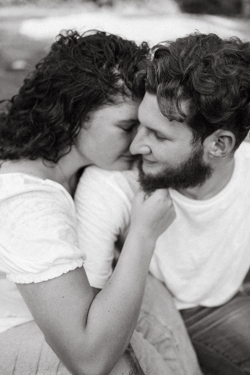 Black and white engagement portrait of woman cuddling into man's neck and him smiling at her during a portrait session. 