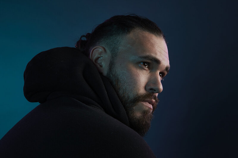 Moody portrait of Nicolai against a deep blue background, captured by Ylva Erevall, highlighting a thoughtful and intense expression.