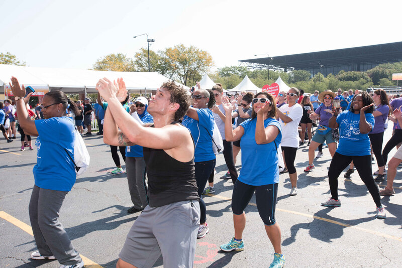 Attendees dancing together in matching shirts at outdoor charity walk with Charizma DJ