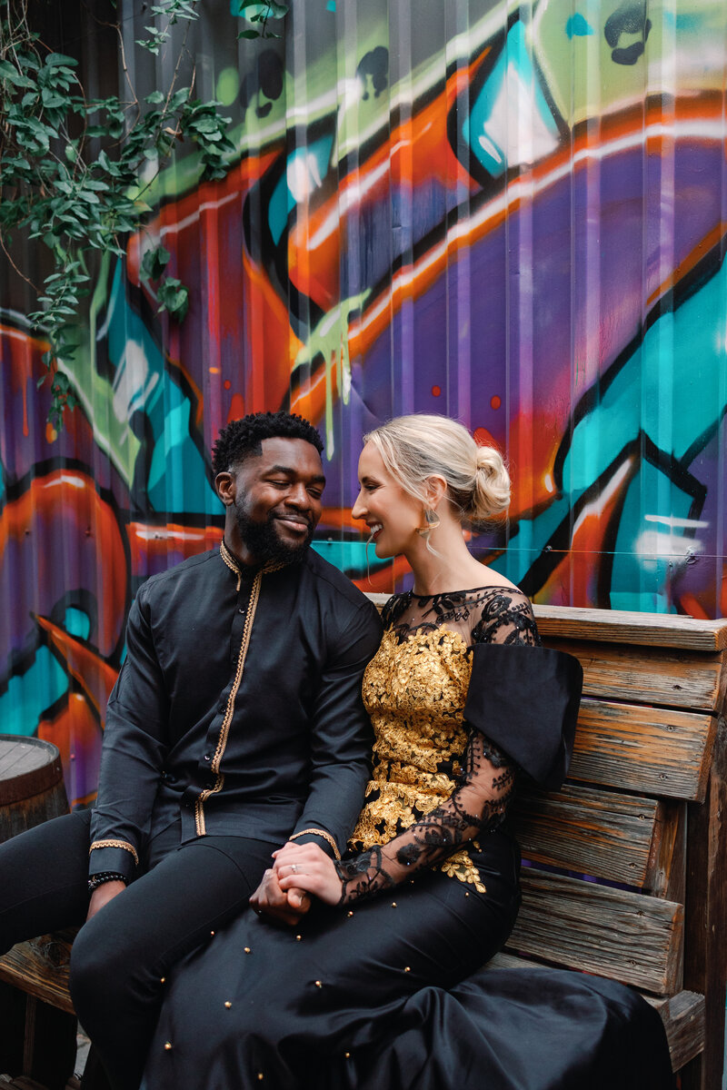 A couple sits outside their wedding on a bench in front of a graffiti background