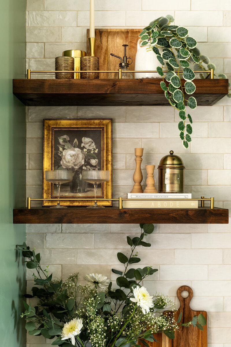 Custom built floating shelves in kitchen decorated with faux plants, glassware, frames, books and kitchen storage canisters.