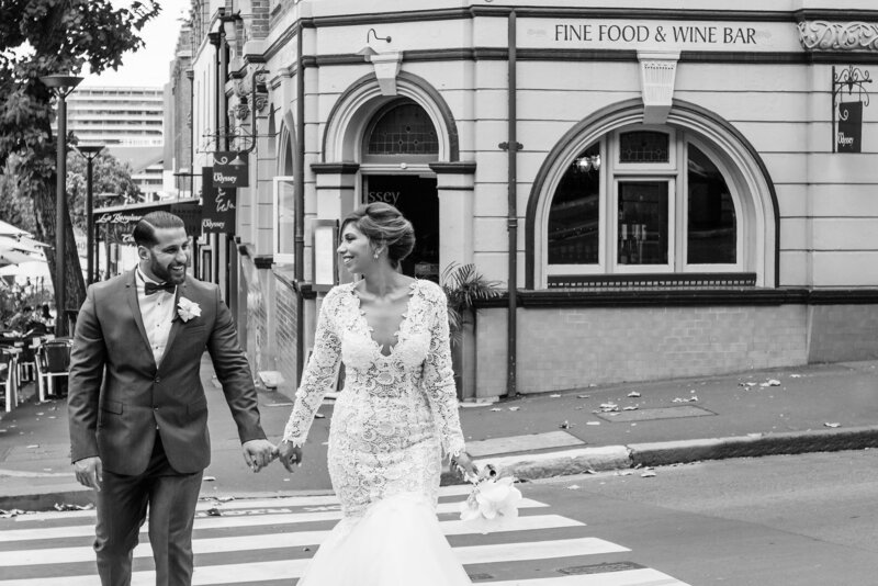 Beautiful wedding day weather as the bride and groom cross the street with their pinky fingers locked