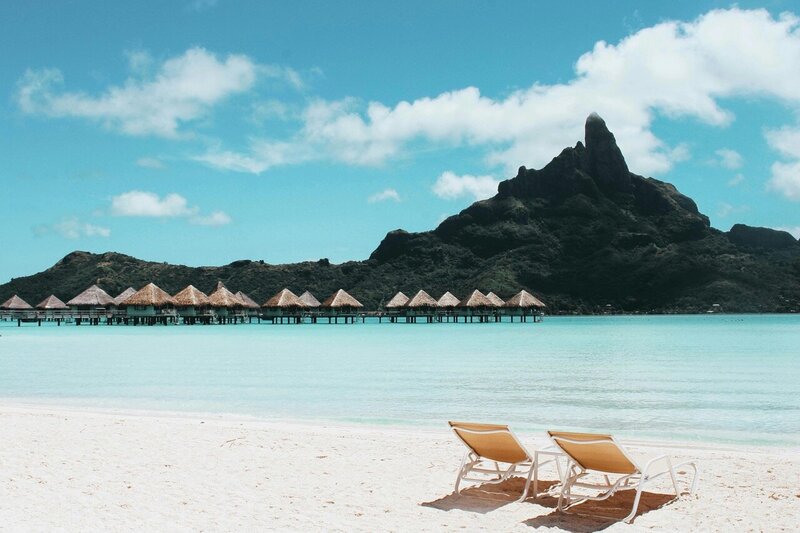 two chairs positioned on a white sand beach facing tropical blue waters in the south pacific