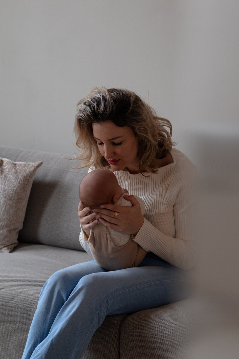 Een vrouw zit op een bank en houdt een baby in haar armen, met een liefdevolle uitstraling op haar gezicht.