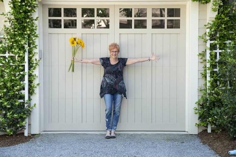 Jane Shine, with her arms open wide holding a bouquet of sunflowers