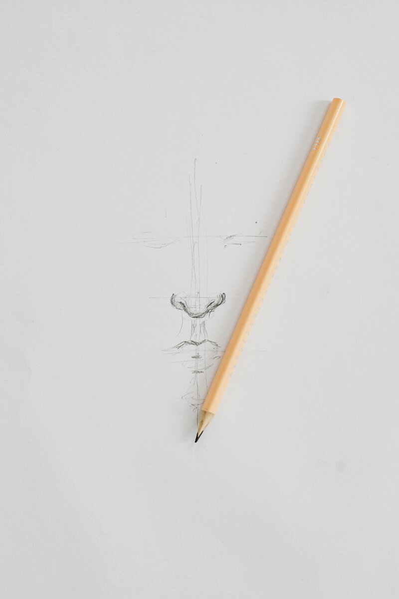 A pencil lays on a white surface next to a rough sketch of a vase or goblet.