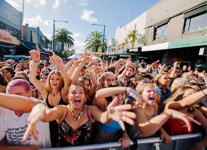 Festival-goers cheering and raising hands in an energetic crowd during a live performance at St Kilda Festival