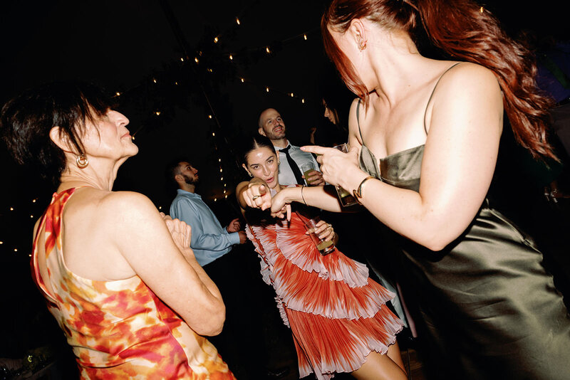 Fun wedding guest in bright dress pointing to the camera dancing at wedding reception