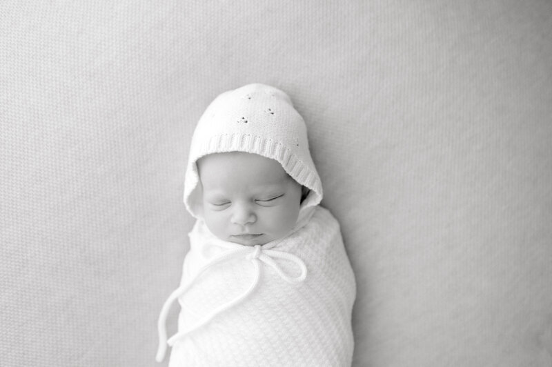 Black and white image of newborn baby swaddled with a bonnet