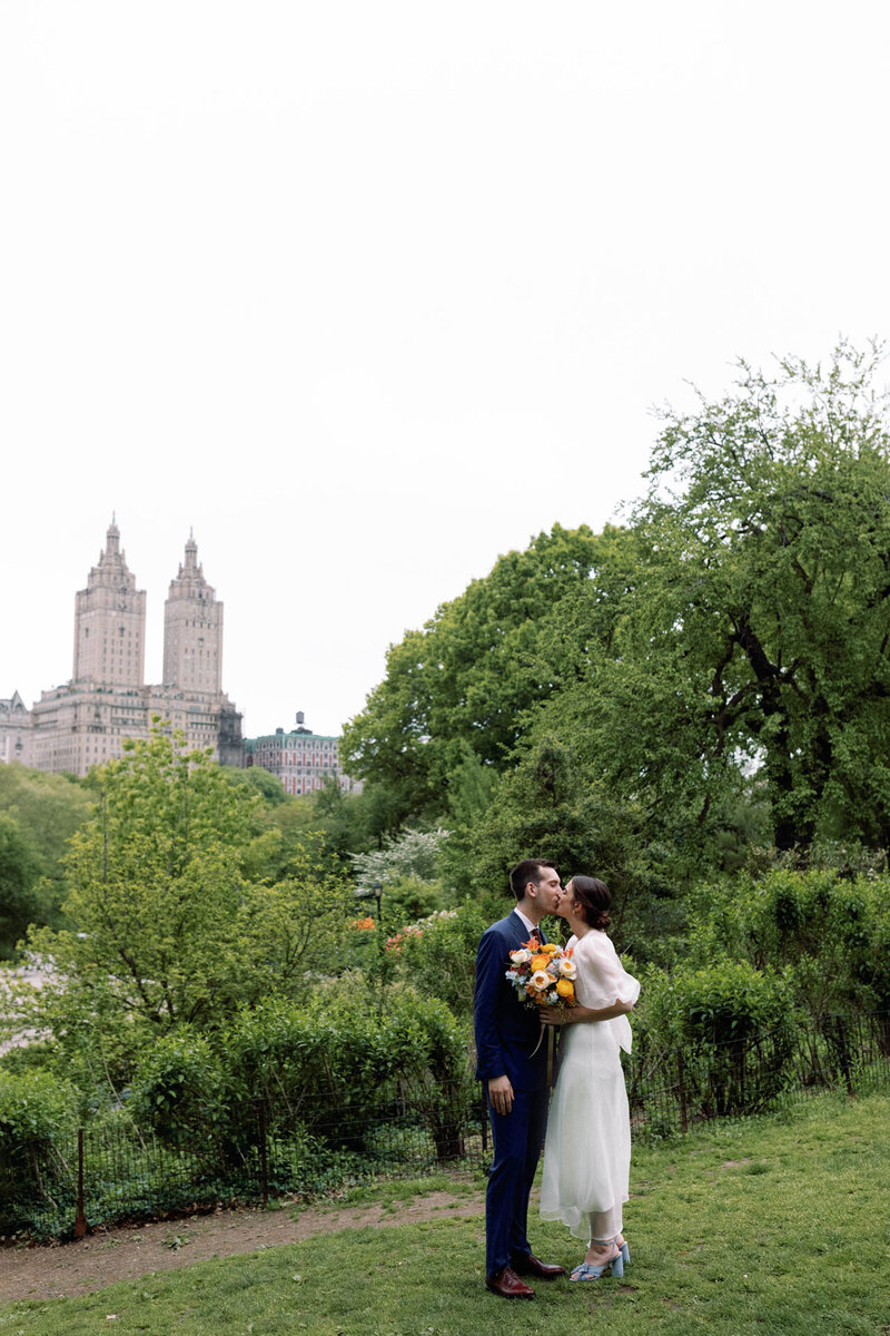 NYC elopement couple in central park kissing with flowers and san remo