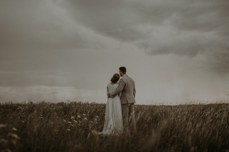 Bride and groom in a field watching the rain rollin on their wedding day.