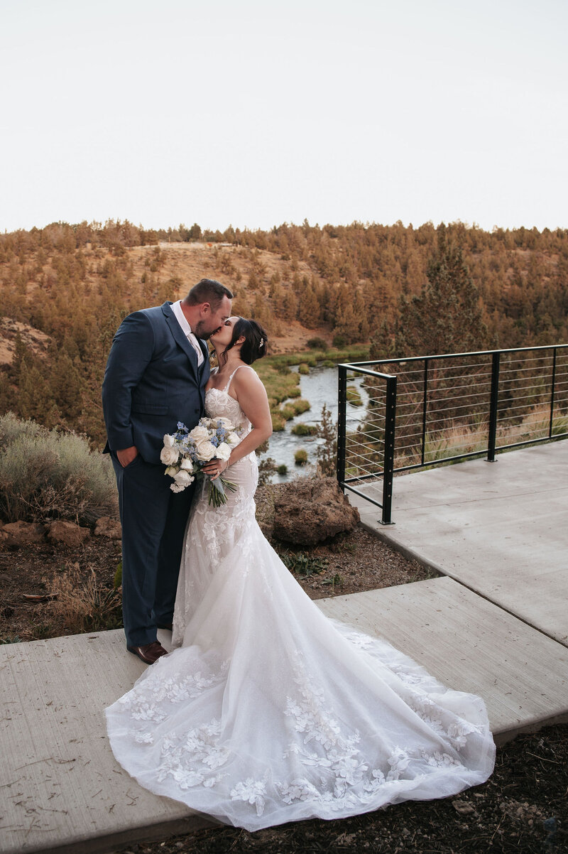A couple shares romantic wedding photos on a paved pathway with scenic golden hour foliage and a river view in the background at River Run Lodge, perfect for outdoor wedding photography in Oregon.