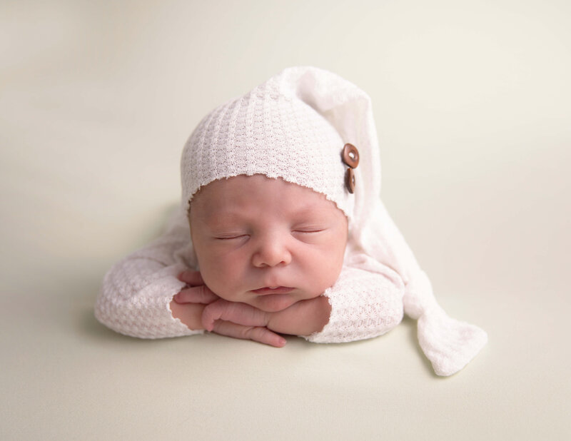 Newborn photo of a baby boy in a white sleeper with a sleepy cap in an Erie Pa photography studio