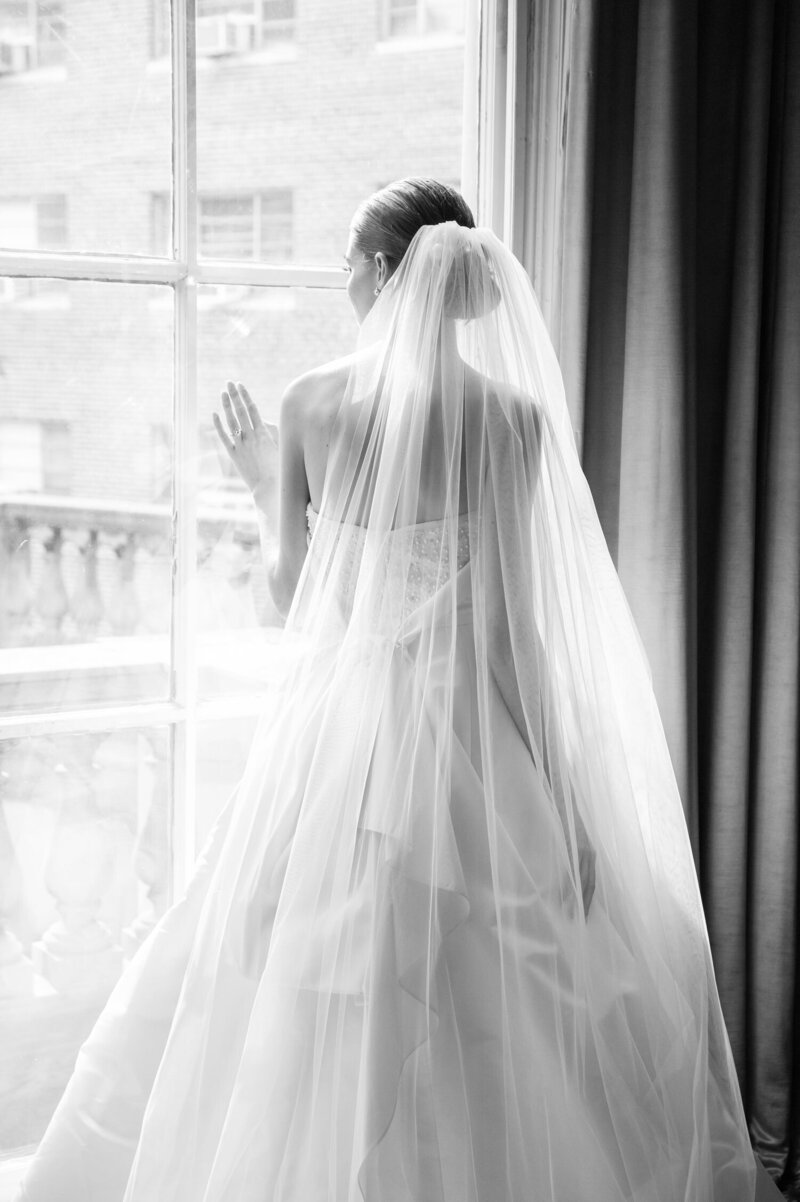 A bride gazes out the large window with her hand on the glass before her Grand Rapids wedding