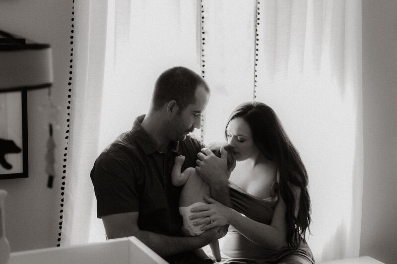 Parents admiring their newborn baby together in the nursery, captured in timeless black and white.