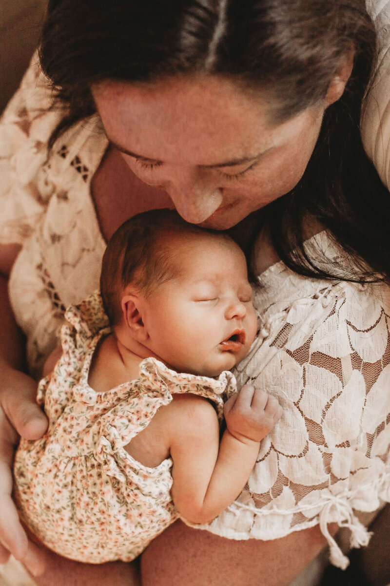 Mom snuggling sleeping baby during in-home newborn photo session.
