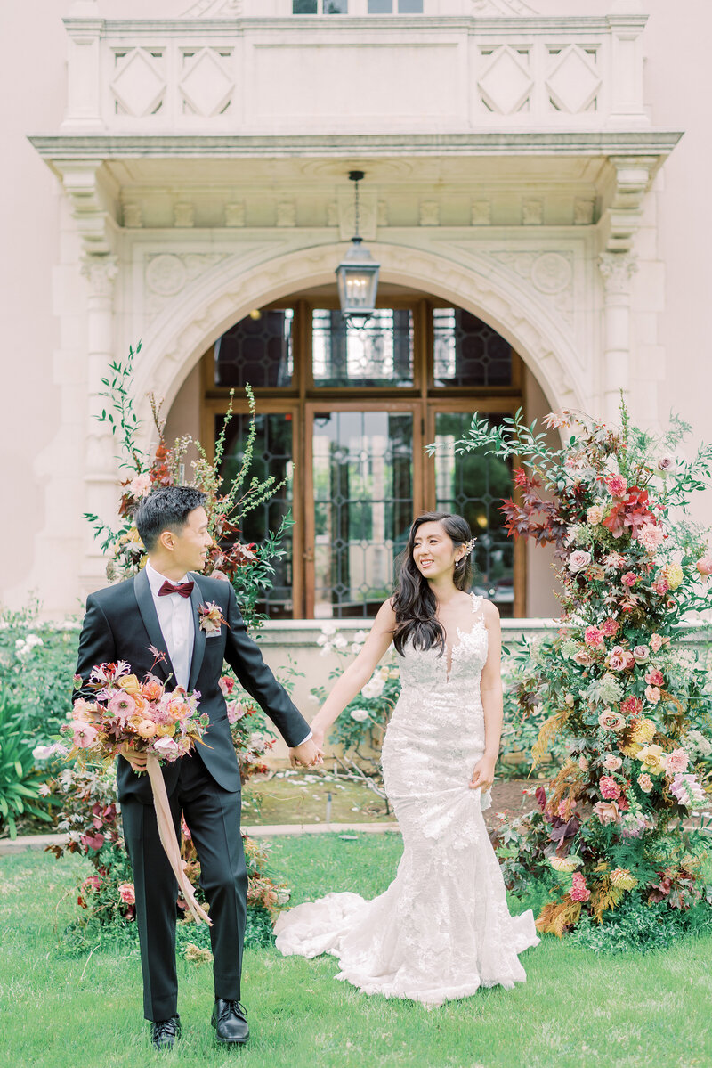 19-alisonbrynn-Radiant-LoveEvents-Maxwell-1-House-groom-leading-bride-holding-hands-in-front-of-floral-columns-outdoors-romantic-elegant-timeless